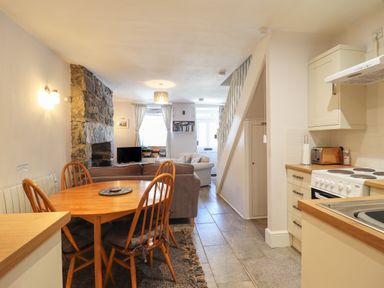 A kitchen and dining area with wooden table and chairs next to a living room with stone fireplace at Llygoden Cottage in Beddgelert
