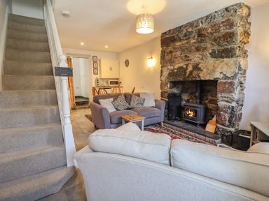 A living room with sofas and a wood burning stove next to a stone fireplace with stairs on the left at Llygoden Cottage in Beddgelert