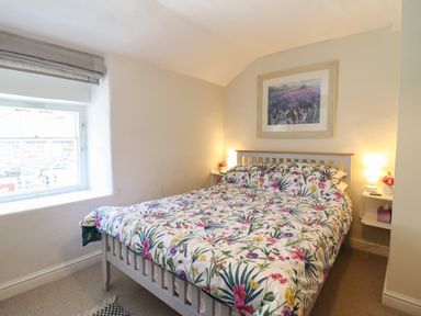 A bedroom with a floral bedspread a window a framed picture and bedside tables with lamps at Llygoden Cottage in Beddgelert