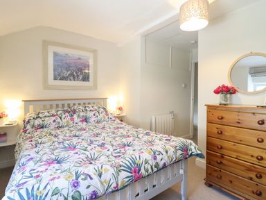 A bedroom with a bed with floral bedding a wooden dresser with a round mirror and a painting on the wall at Llygoden Cottage in Beddgelert