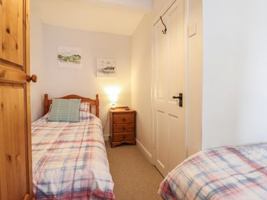 A small bedroom with two single beds a wooden wardrobe and a bedside table with a lamp at Llygoden Cottage in Beddgelert