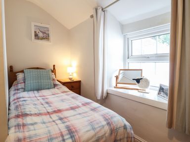 A small bedroom with a single bed wooden nightstand with a lamp window with curtains and decorative items on the windowsill at Llygoden Cottage in Beddgelert