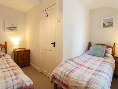 A bedroom with two single beds a wooden nightstand and framed pictures on the walls at Llygoden Cottage in Beddgelert