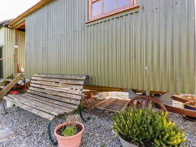 An outdoor area with a wooden bench and potted plants beside a corrugated metal shed on wheels at Puddle Duck Shepherds Hut in Crackington Haven