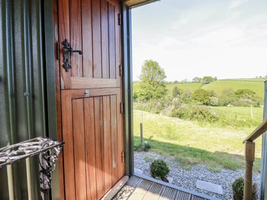 An open wooden door leading to a grassy field and trees at Puddle Duck Shepherds Hut in Crackington Haven