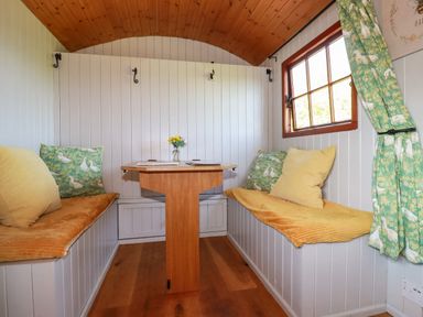 A small dining area with two cushioned benches and a wooden table under a wooden ceiling at Puddle Duck Shepherds Hut in Crackington Haven