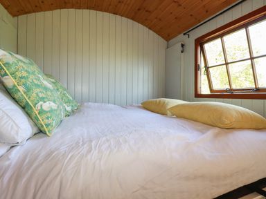 A bed with pillows next to a window in a wood-paneled room at Puddle Duck Shepherds Hut in Crackington Haven