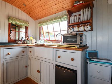 A kitchen corner with cabinets a countertop toaster oven and a wooden plate rack at Puddle Duck Shepherds Hut in Crackington Haven