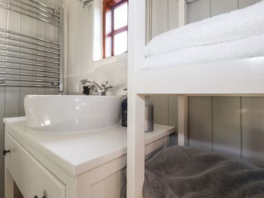 A bathroom sink with a faucet next to a window and shelf with towels and toiletries at Puddle Duck Shepherds Hut in Crackington Haven