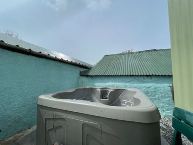 An outdoor hot tub next to turquoise walls and green corrugated metal roofs at Puddle Duck Shepherds Hut in Crackington Haven