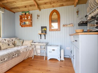 A small living space with a couch, a side table, a stove, a mirror, shelves, and kitchen cabinets at Shepherds Retreat in Maxworthy near Crackington Haven