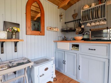 A small kitchen with blue cabinetry a wooden countertop a toaster oven a kettle hanging pots and cups and a small stove at Shepherds Retreat Maxworthy near Crackington Haven