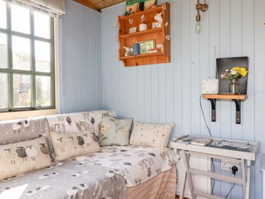 A corner with a sofa covered with sheep patterned blankets and cushions beside a window and a wall shelf at Shepherds Retreat in Maxworthy near Crackington Haven