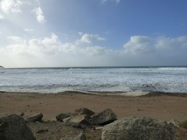 A sandy beach with rocks in the foreground and waves in the ocean under a cloudy sky at Shepherds Retreat in Maxworthy near Crackington Haven