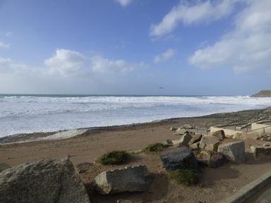 A beach with rocks and a sandy shore next to the sea with waves and cloudy sky at Shepherds Retreat in Maxworthy near Crackington Haven