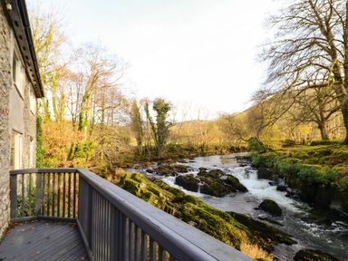 A balcony with a wooden railing overlooking a river with rocks and trees at Pen y Bont Near Mallwyd