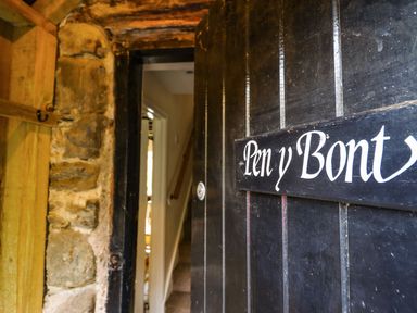 A partially open black door with a sign reading Pen y Bont showing an entrance with stone walls and a view inside revealing a hallway and stairs at Pen y Bont Near Mallwyd