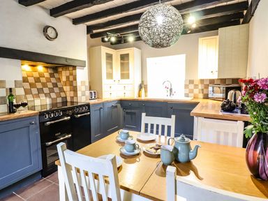 A kitchen with blue cabinets wooden countertops a dining table with tea set and flowers at Pen y Bont Near Mallwyd