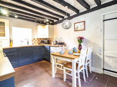 A kitchen with dark blue lower cabinets and white upper cabinets a wooden dining table with white chairs and a flower vase at Pen y Bont Near Mallwyd