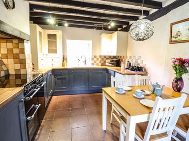 A kitchen with blue cabinets wooden countertops a dining table with teapot cups and flowers at Pen y Bont Near Mallwyd