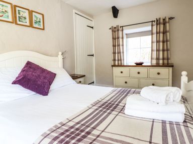 A bedroom with a white bed and purple pillow next to a dresser under a window at Pen y Bont Near Mallwyd
