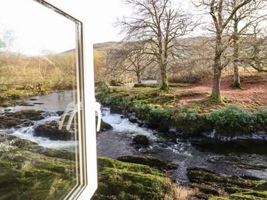 A river with rocks and moss beside trees with bare branches seen through an open window at Pen y Bont Near Mallwyd