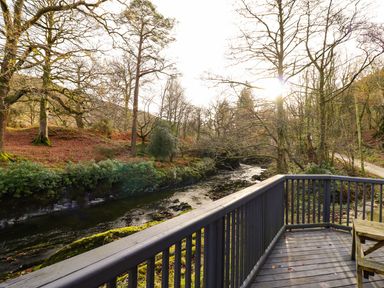 A wooden deck overlooking a river surrounded by trees and a dirt path at Pen y Bont Near Mallwyd