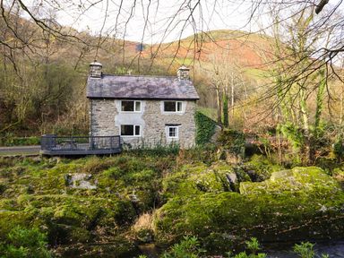 A stone house with a deck surrounded by trees and mossy rocks at Pen y Bont Near Mallwyd