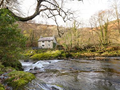 A stone house near a river with mossy rocks and leafless trees in a wooded area at Pen y Bont Near Mallwyd