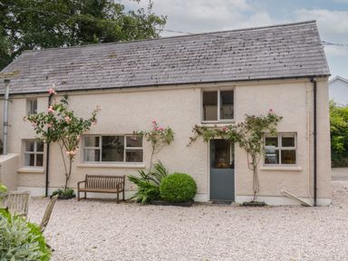 Exterior of a beige stucco house with a gray door and windows with rose plants growing beside the door at The Old Rectory Coach House in Rathmullan County Donegal