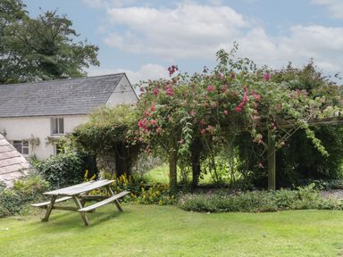 A wooden picnic table on grass near a pergola with climbing pink flowers and a house in the background at The Old Rectory Coach House in Rathmullan County Donegal