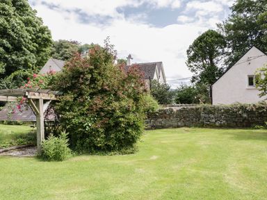 A garden with a wooden pergola a bush stone wall and houses in the background at The Old Rectory Coach House in Rathmullan County Donegal