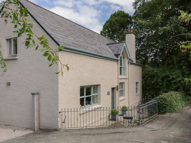 An exterior view of a beige house with blue window frames a small fenced patio with plants and chairs at The Old Rectory Coach House Rathmullan County Donegal
