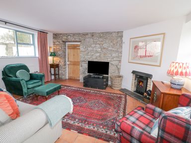 A living room with a stone wall a wooden door a television a fireplace and patterned rugs at The Old Rectory Coach House in Rathmullan County Donegal