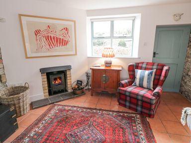 A sitting room with a red plaid armchair a wooden cabinet with a lamp a fireplace and a patterned rug at The Old Rectory Coach House in Rathmullan County Donegal