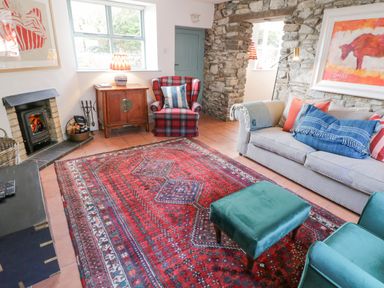 A living room with a red patterned rug a beige sofa with cushions a teal armchair and ottoman a stone wall and a small fireplace at The Old Rectory Coach House in Rathmullan County Donegal