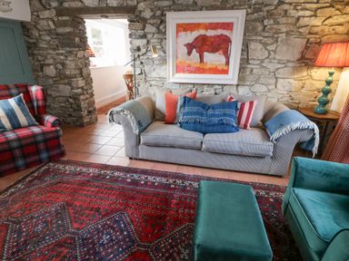 A living room with a stone wall a sofa with pillows a red patterned rug and a plaid armchair at The Old Rectory Coach House in Rathmullan County Donegal