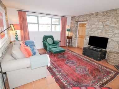 A living room with a sofa and green armchair facing a television on a black stand and a red patterned rug on the floor at The Old Rectory Coach House in Rathmullan County Donegal