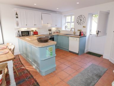 A kitchen with light blue lower cabinets white upper cabinets wooden countertops and terracotta floor tiles at The Old Rectory Coach House in Rathmullan County Donegal