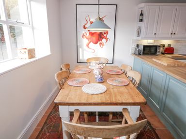 A dining area with a wooden table and six chairs placed near a kitchen with blue cabinets and a countertop at The Old Rectory Coach House in Rathmullan County Donegal