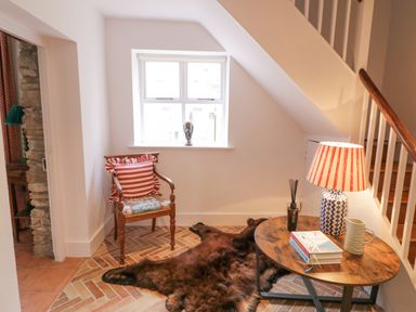 A sitting area with a wooden chair with cushions a round wooden table with a lamp books and a pitcher and a dark fur rug on a brick patterned floor at The Old Rectory Coach House in Rathmullan County Donegal
