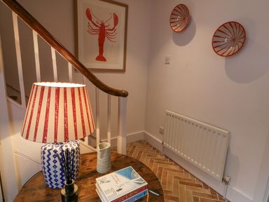A staircase corner with a wooden railing a striped lamp on a round wooden table books on the table a framed lobster print on the wall and two decorative red bowls on the wall at The Old Rectory Coach House in Rathmullan County Donegal