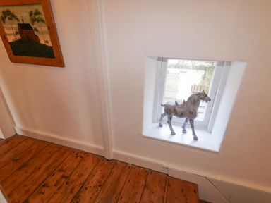 A small window with a horse figurine on the sill and a painting on the wall above wooden floorboards at The Old Rectory Coach House in Rathmullan County Donegal