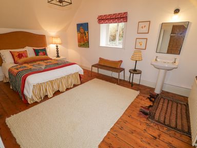 A bedroom with a bed a bedside lamp a mirror a sink a window and rugs on the wooden floor at The Old Rectory Coach House in Rathmullan County Donegal