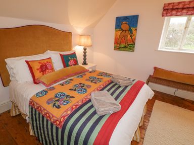 A bedroom with a bed covered with colorful bedspread and pillows plus a lamp on a side table a painting on the wall and a window at The Old Rectory Coach House in Rathmullan County Donegal