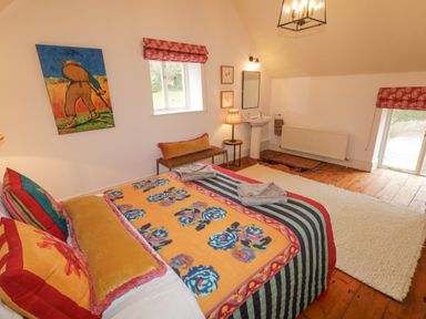 A bedroom with a bed with colorful bedding a wall painting a small window and a washbasin at The Old Rectory Coach House in Rathmullan County Donegal
