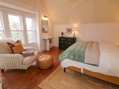 A bedroom with a bed a green blanket a black dresser a checkered armchair and a washbasin at The Old Rectory Coach House in Rathmullan County Donegal