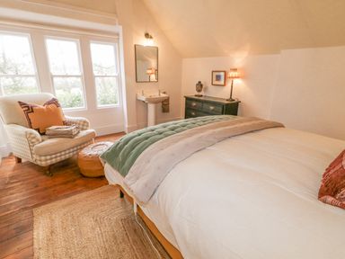 A bedroom with a bed pillows and blanket armchair with cushions small sink black dresser with lamp and bust at The Old Rectory Coach House in Rathmullan County Donegal