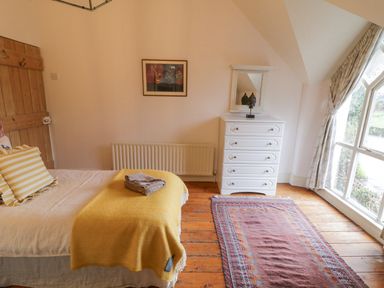A bedroom with a bed covered by a yellow blanket and pillow a white chest of drawers with a mirror and a carpet on wooden floor at The Old Rectory Coach House in Rathmullan County Donegal