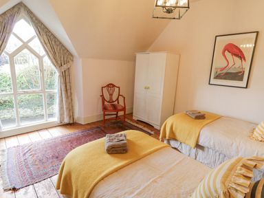 A bedroom with two single beds with yellow blankets a wooden chair a white wardrobe a framed flamingo picture and a large window at The Old Rectory Coach House in Rathmullan County Donegal